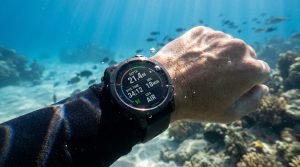 Une montre d'ordinateur de plongée au poignet sous l'eau affichant la profondeur et le temps de plongée.