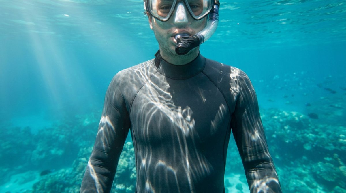 Un plongeur portant une combinaison néoprène et un masque de plongée sous l'eau dans une mer tropicale claire.